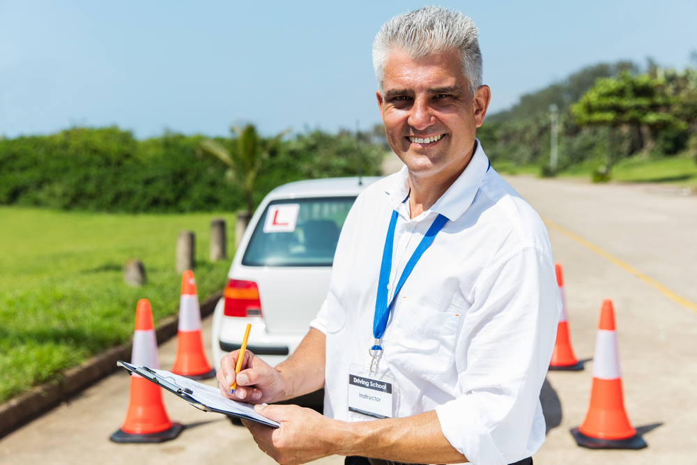 a male driving instructor holding a clipboard in front of a car